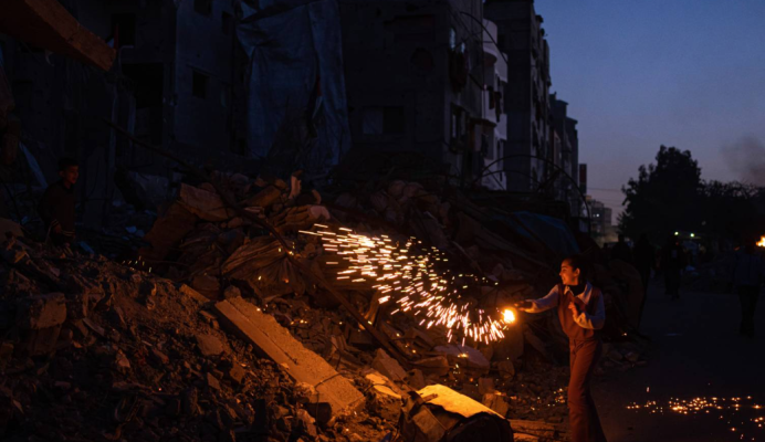 Një fëmijë luan me fishekzjarre ndërsa feston fillimin e Ramazanit pranë një ndërtese banimi të dëmtuar në Rafah [AP/ Fatima Shbair].